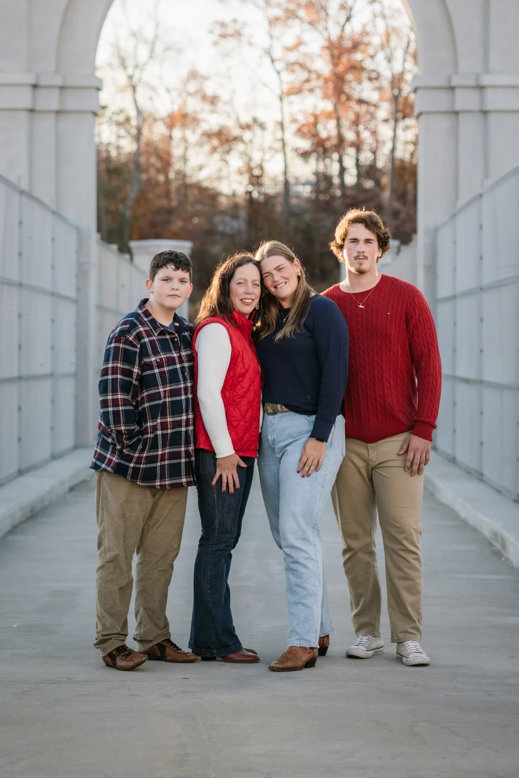 The Garman's family photos taken at BridgeWay Station, Simpsonville: Group portrait of four people standing close together on a concrete pathway under an archway with trees in the background.
