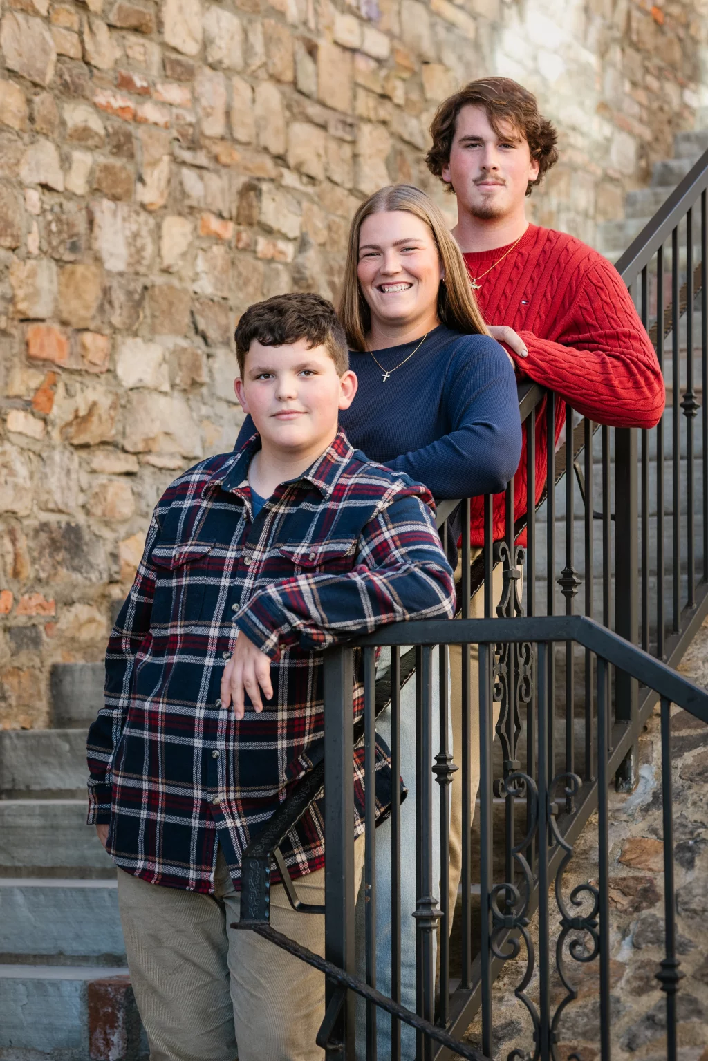 The Garman's family photos taken at BridgeWay Station, Simpsonville: Three people posing on an outdoor stone staircase leaning on a black iron railing, smiling and facing the camera.