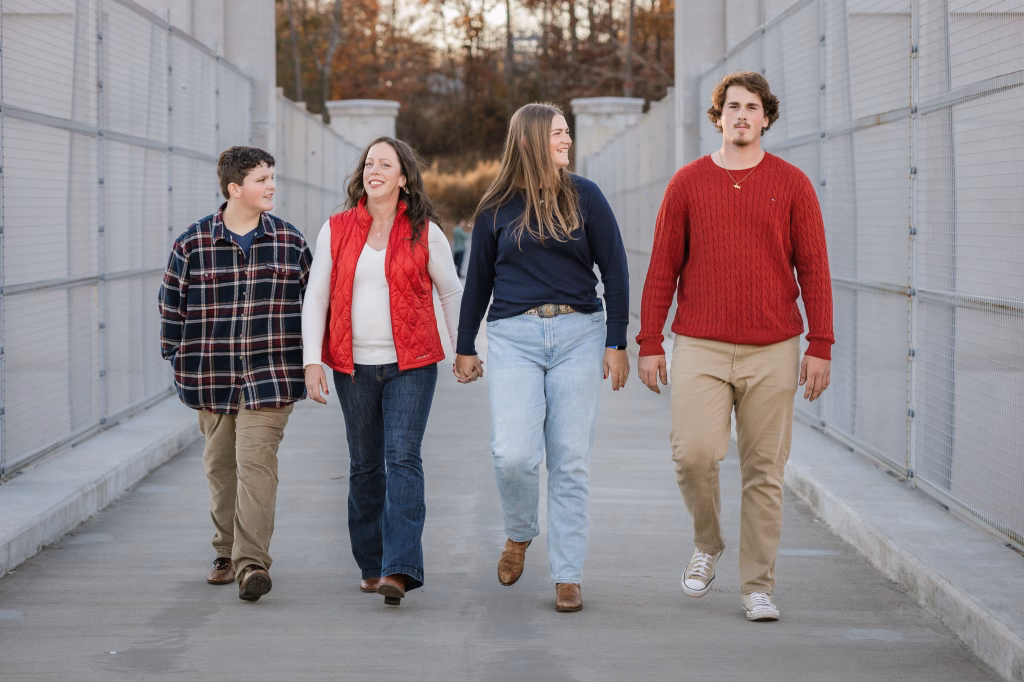 The Garman family photos taken at BridgeWay Station, Simpsonville: Four people walking down a fenced pathway, two women holding hands in the middle, flanked by two men, all smiling and casually dressed.