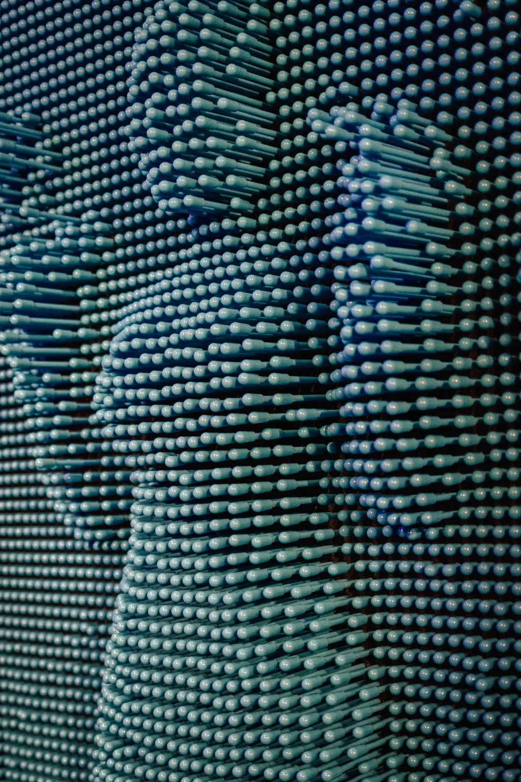 : Close-up of a pin art board, showing the impression of a person with raised hands formed by numerous blue pins.