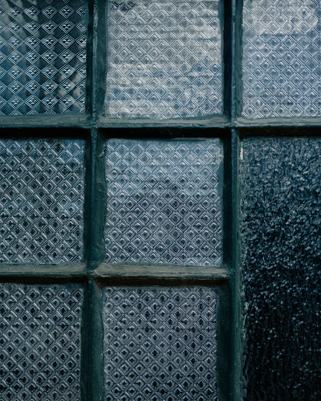 : Close-up of a window with textured, patterned glass panes divided by dark metal muntins.