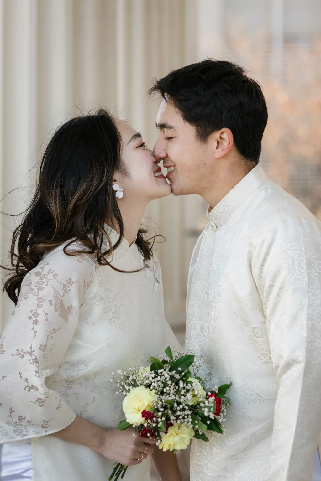 Robby and Hannah's couple photo session taken Downtown, Greenville: Close-up of a smiling couple wearing traditional white attire, about to kiss, with the woman holding a bouquet of flowers.