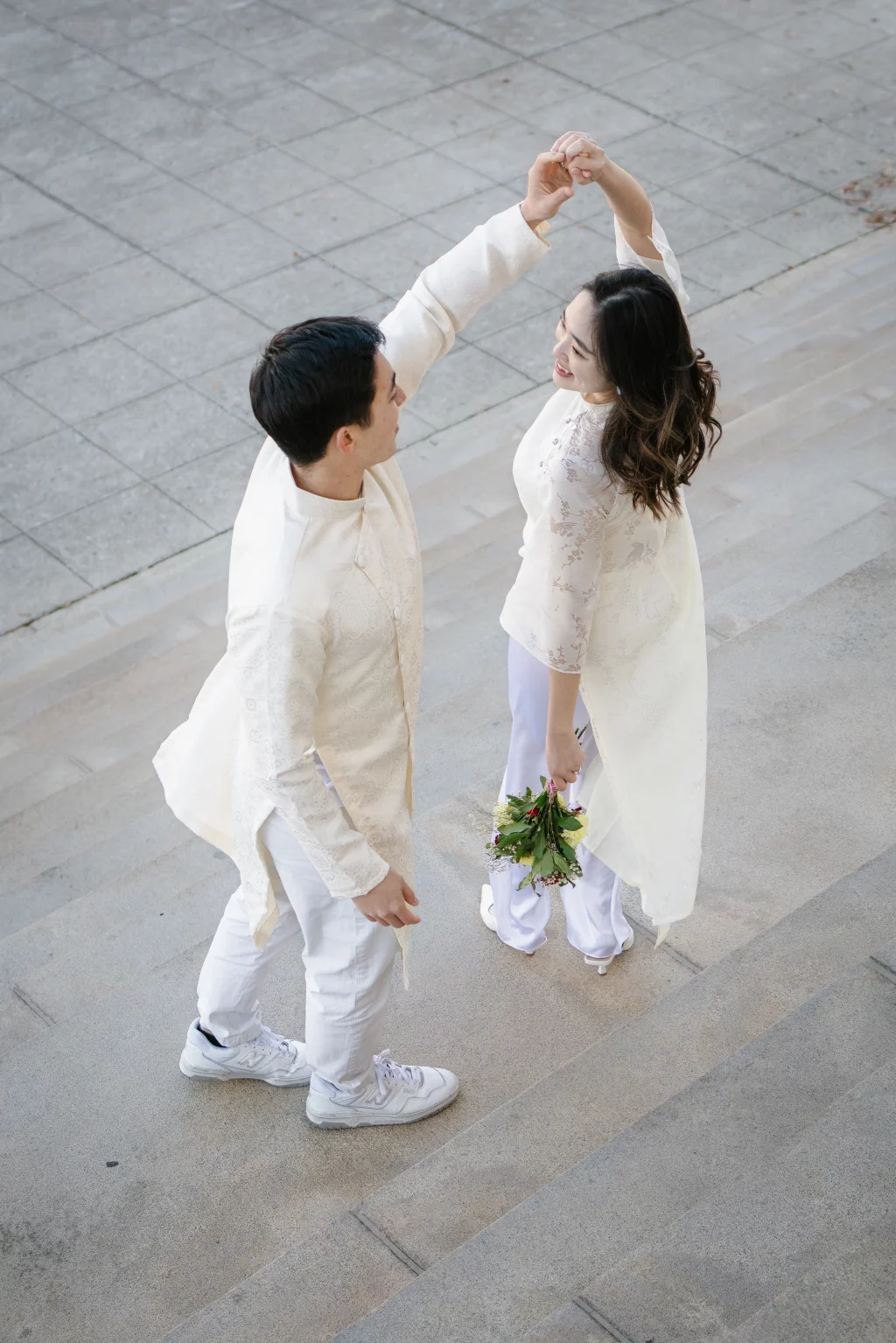 Robby and Hannah's couple photo session taken Downtown, Greenville: Couple dressed in traditional white attire dancing on stone steps, woman holding a small bouquet of flowers.