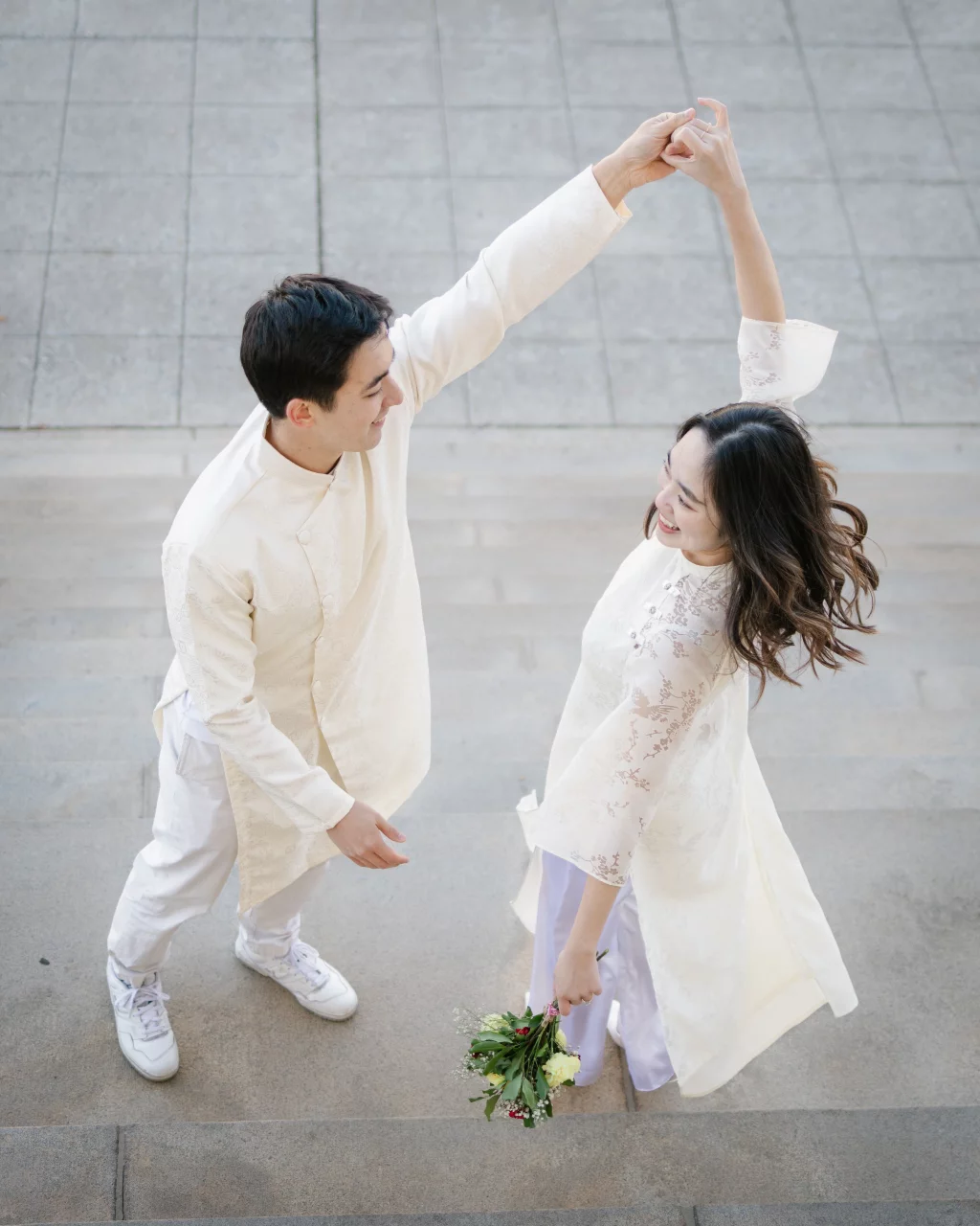 Robby and Hannah's couple photo session taken Downtown, Greenville: Couple in traditional white attire dancing on stone steps, woman holding bouquet, smiling at each other.