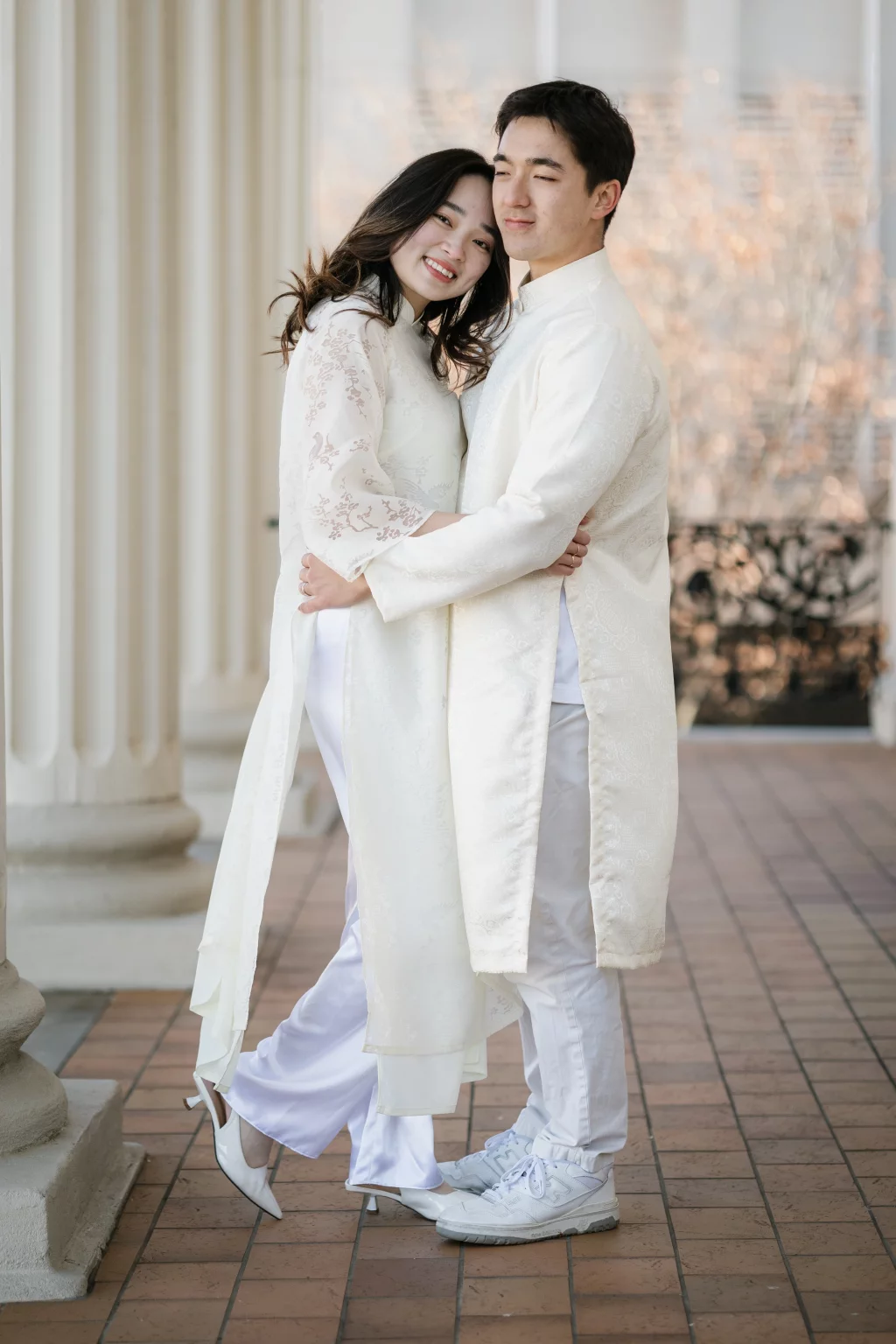 Robby and Hannah's couple photo session taken Downtown, Greenville: Young couple in matching traditional white attire embracing on a tiled porch with white columns.