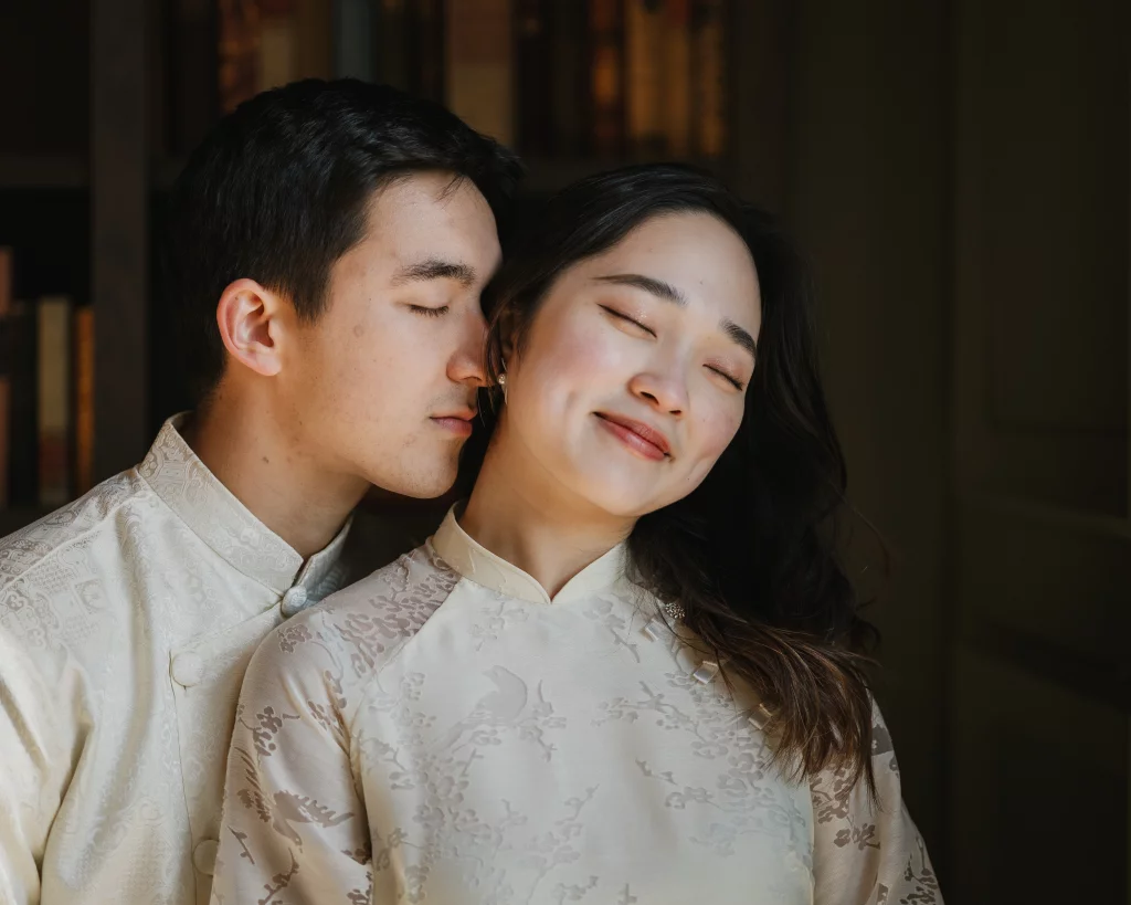 Robby and Hannah's couple photo session taken Downtown, Greenville: Close-up of a couple in traditional beige silk attire, the man gently resting his face near the woman's cheek, both with eyes closed and serene smiles.