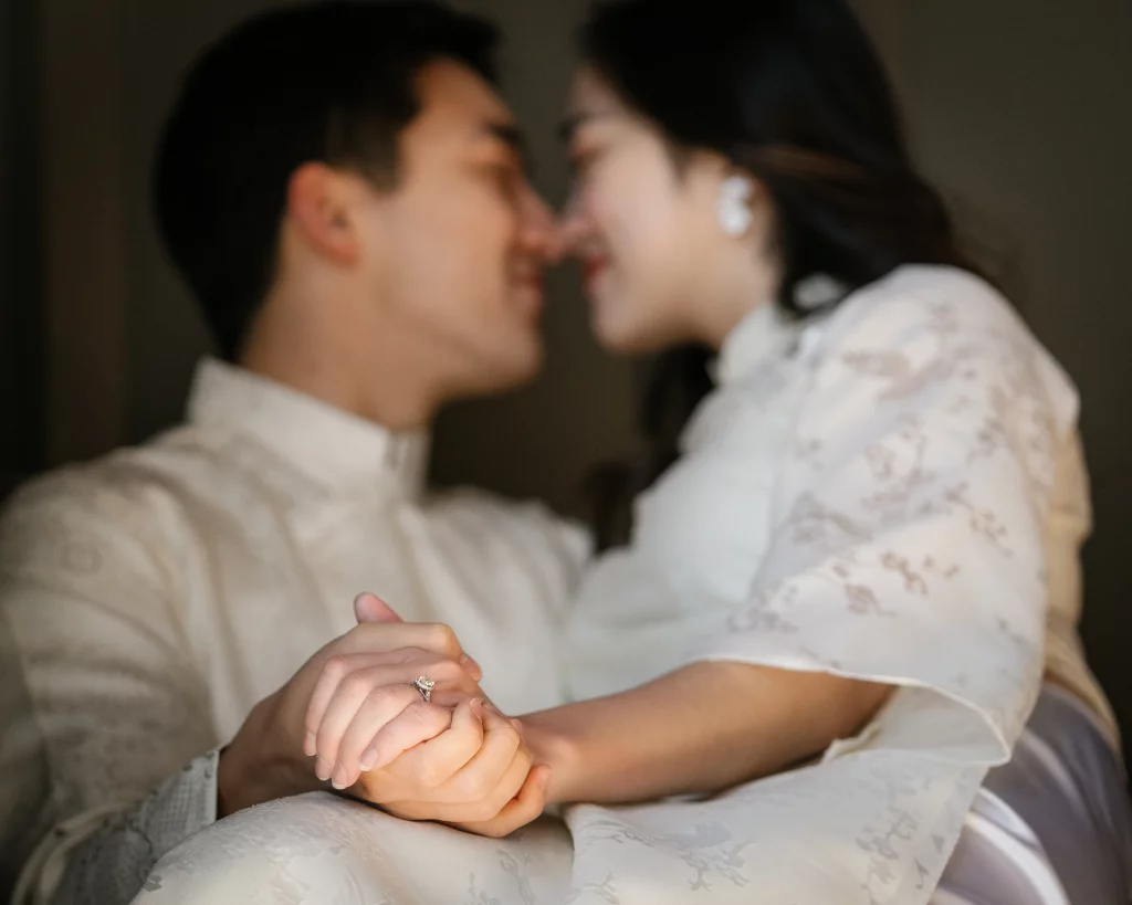Robby and Hannah's couple photo session taken Downtown, Greenville: Close-up of a couple holding hands with an engagement ring visible, faces close together and blurred in the background.