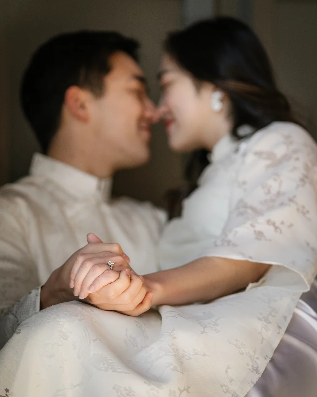 Robby and Hannah's couple photo session taken Downtown, Greenville: Blurred close-up of a couple in traditional clothing holding hands showing an engagement ring, touching noses affectionately.