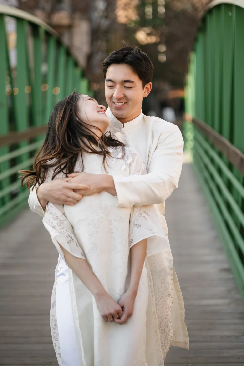 Robby and Hannah's couple photo session taken Downtown, Greenville: Couple in traditional white attire embracing on a green bridge, smiling and looking at each other.