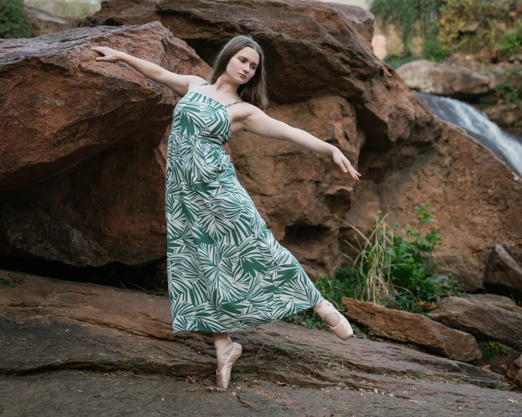 Sabrina's senior photos taken downtown Greenville, SC: Ballet dancer in green and white leaf-patterned dress posing on pointe shoes outdoors against large rocks and a small waterfall.