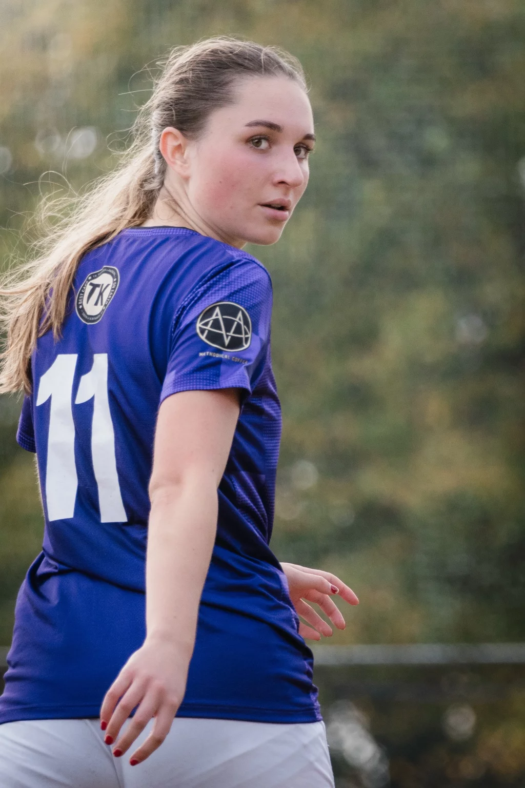 United FC - Furman Region -: A female soccer player with a ponytail, wearing a blue jersey with the number 11 and white shorts, looks over her shoulder during an outdoor game.