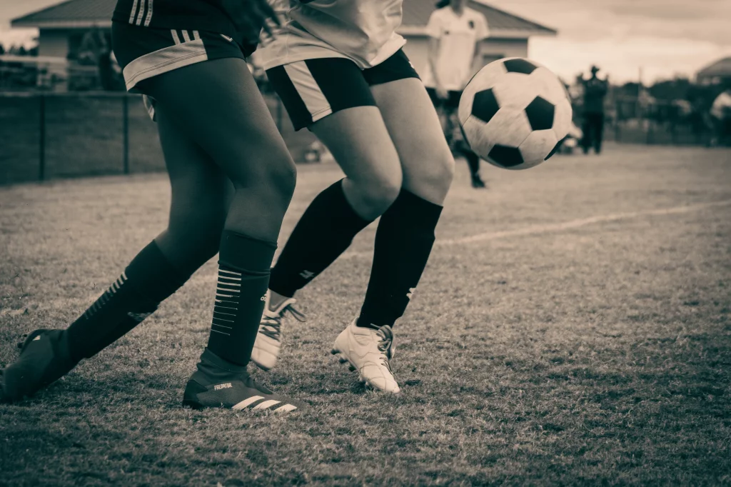 : Close-up of two soccer players&rsquo; legs in action, competing for the ball on a grassy field.