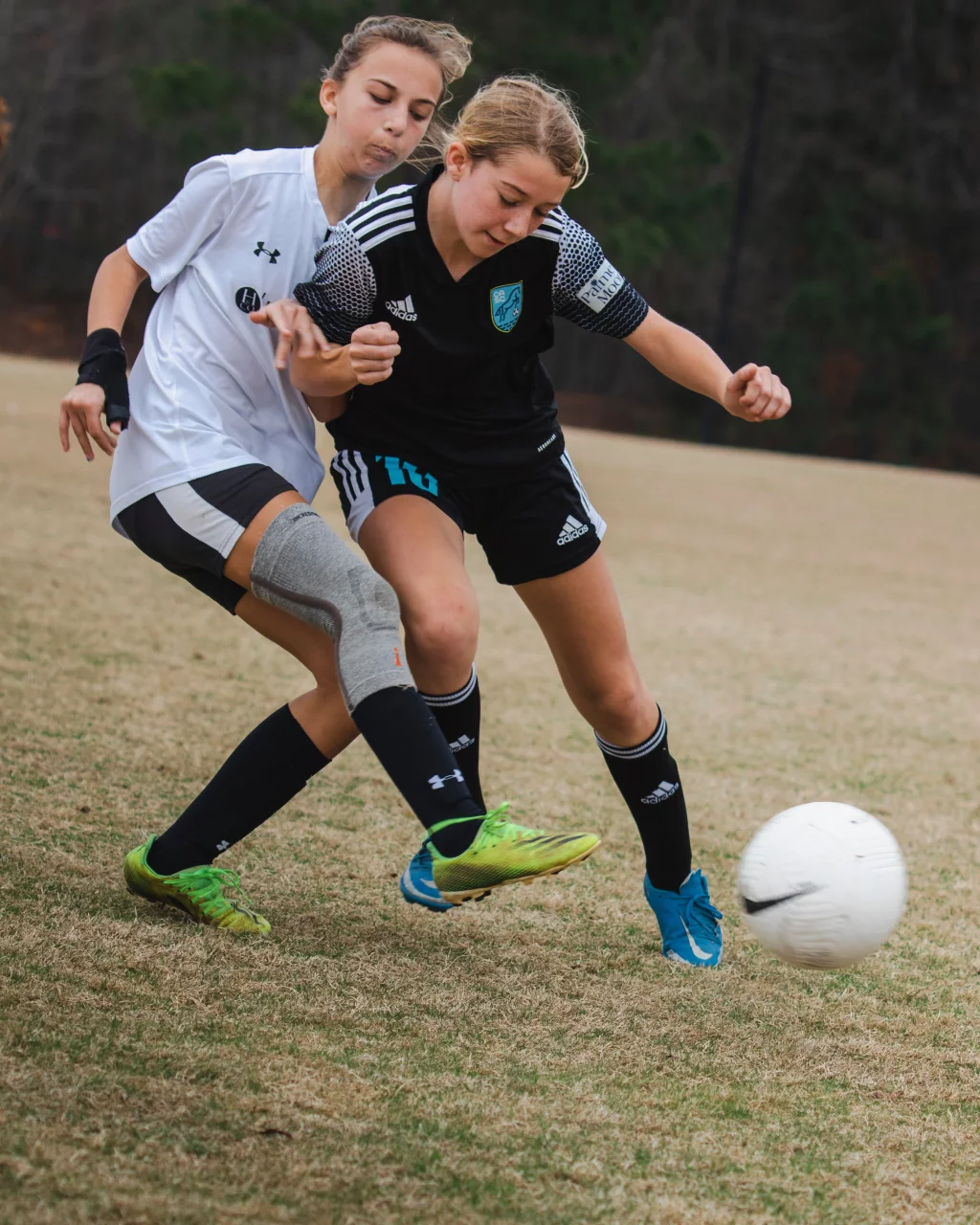 United FC - Furman Region -: Two youth soccer players, one in a white uniform and one in a black uniform, compete closely for the ball on a grassy field.