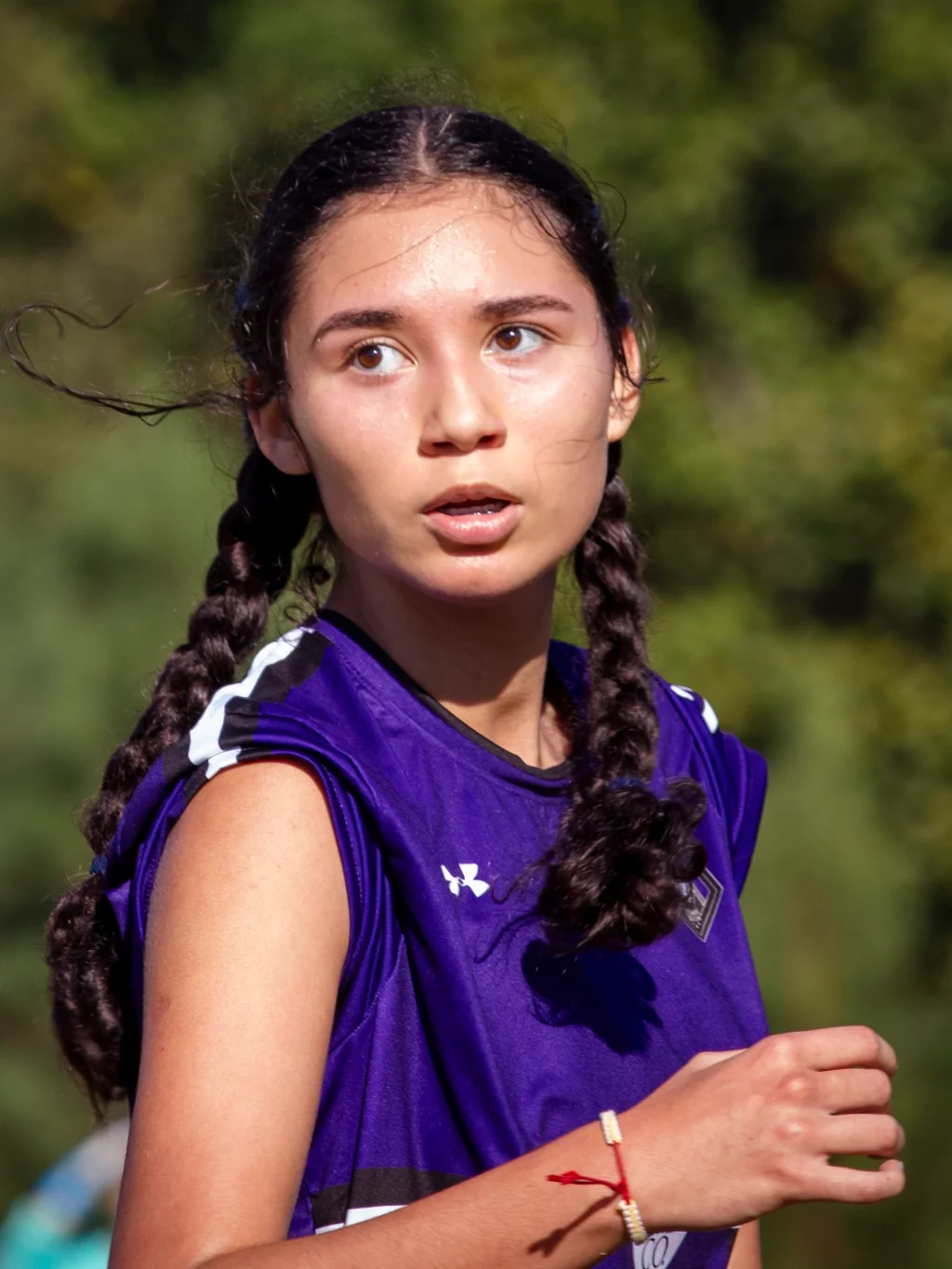 United FC - Furman Region -: A young girl with braided hair wearing a purple sports jersey looks to the side while running outdoors, with a blurred green background.