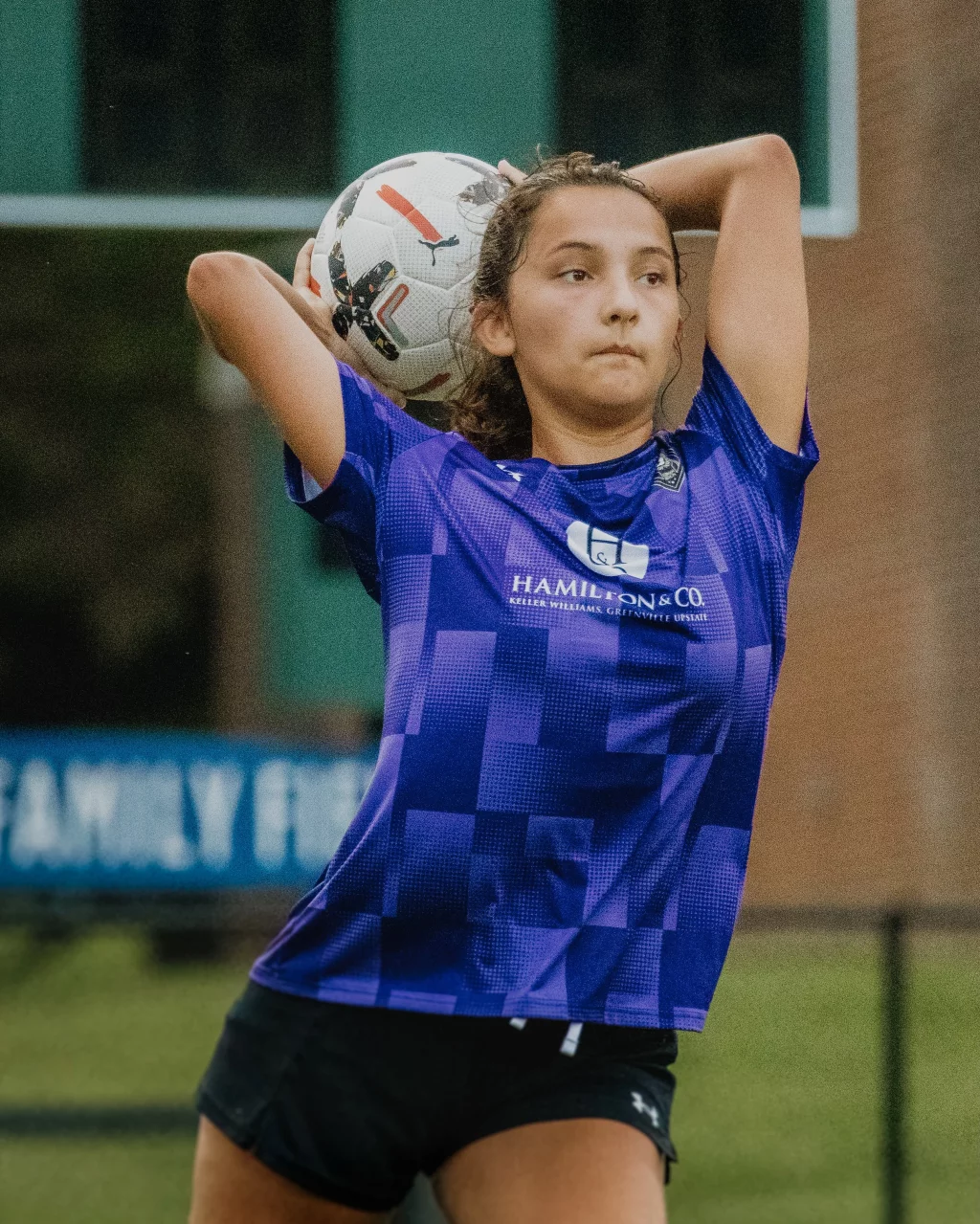 United FC - Furman Region -: A young soccer player in a purple jersey prepares to throw a soccer ball overhead during a game.